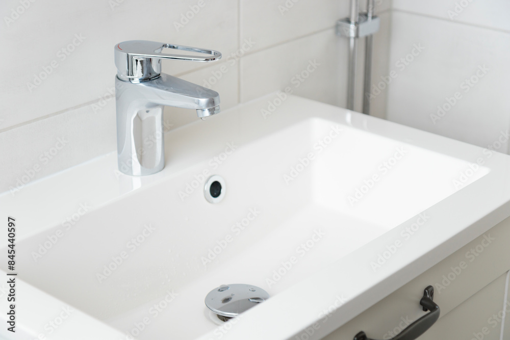 A drop of pure water dripping from the tap in the white modern bathroom. Clean tap water concept. Wise use of natural resources. A drop of pure water dripping from the tap in the white modern bathroom. Clean tap water concept. Wise use of natural resources.