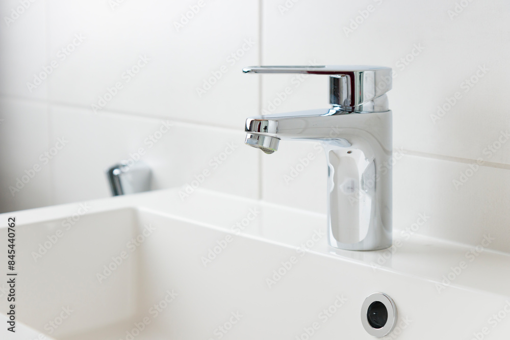 A drop of pure water dripping from the tap in the white modern bathroom. Clean tap water concept. Wise use of natural resources. A drop of pure water dripping from the tap in the white modern bathroom. Clean tap water concept. Wise use of natural resources.