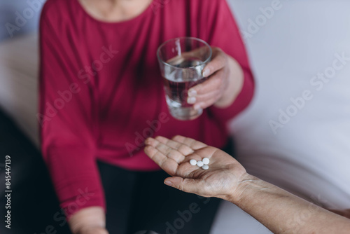An elderly woman sits on her bed and a volunteer gives her pills and a glass of water