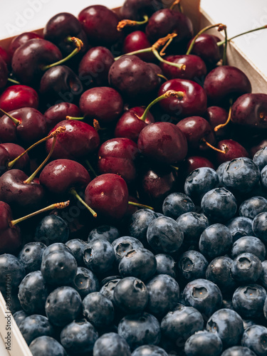 A tray with mix of fresh ripe sweet cherry and blueberries background closeup