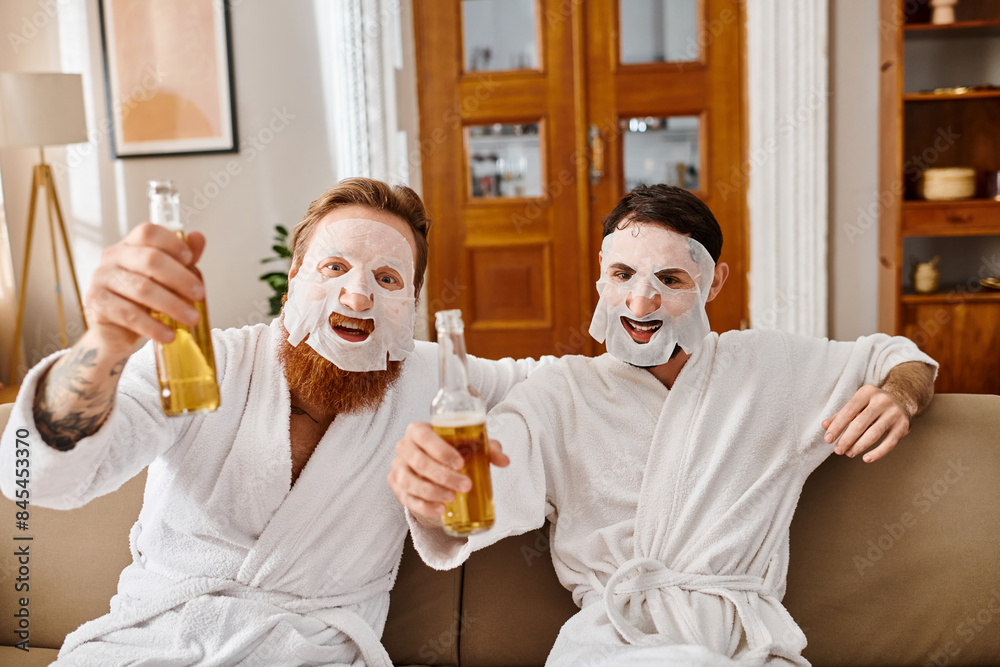 Φωτογραφία Two men in white robes share a fun moment, holding beer and wearing facial masks for a relaxing and enjoyable time together
