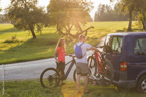 Young man is unloading electric mountain bikes, for himself and his girlfriend, lifting them from the hitch rack on the vehicle. photo