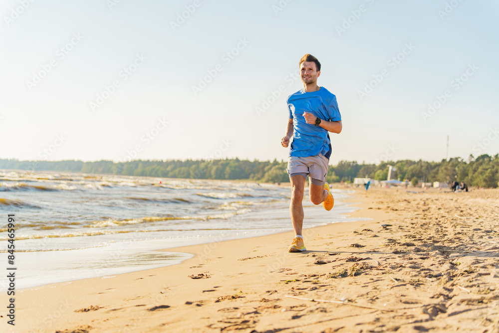 A man runs along a sunny beach near the waves, wearing a blue shirt and bright shoes, smiling as he jogs. A man runs along a sunny beach near the waves, wearing a blue shirt and bright shoes, smiling as he jogs.