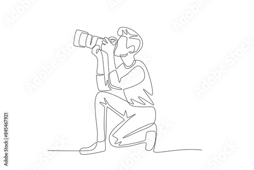 The male photographer who is taking photos is facing upwards while squatting. World photography day concept one-line drawing