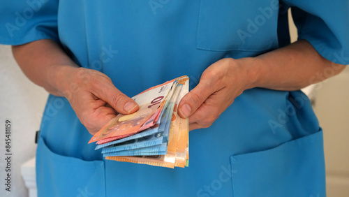 Close-up of the hands of a nurse in a turquoise uniform holding and counting money. Concept of acute shortage of medical personnel. The concept of a good salary for medical and elderly care staff.