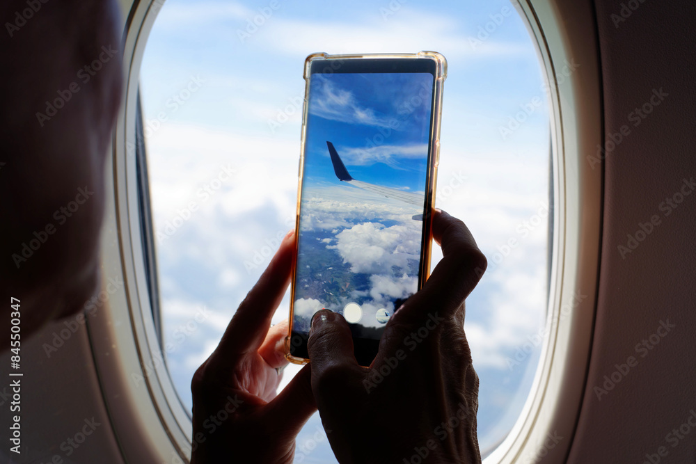 a woman at an aeroplane window holds a smartphone in her hand and takes pictures of the landscape and clouds below her a woman at an aeroplane window holds a smartphone in her hand and takes pictures of the landscape and clouds below her