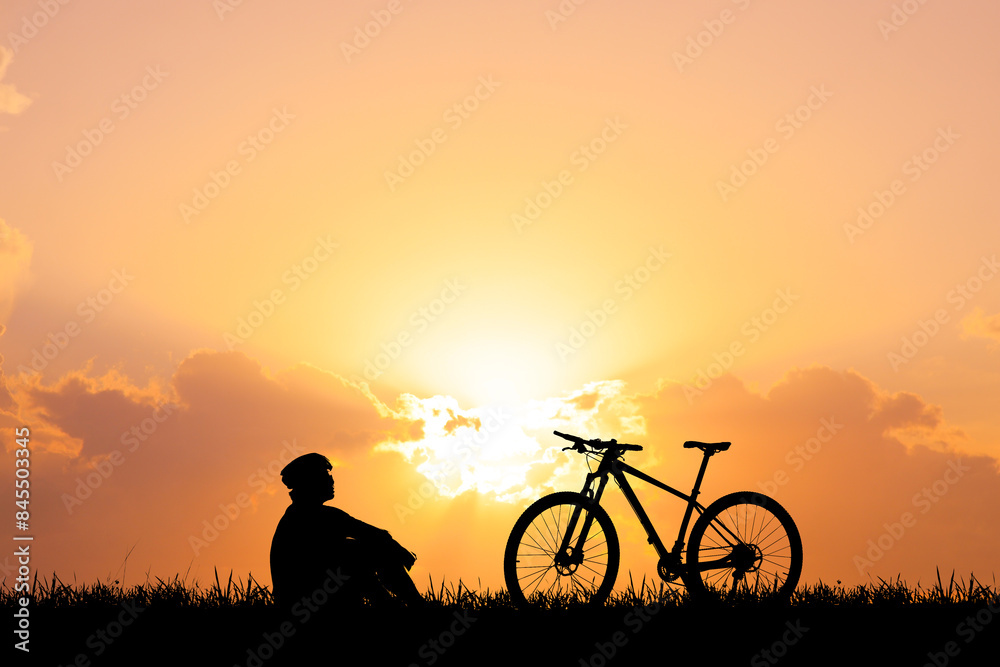 Silhouette of a Person Sitting Next to a Bicycle at Sunset with a Vibrant Orange Sky and Clouds in the Background
