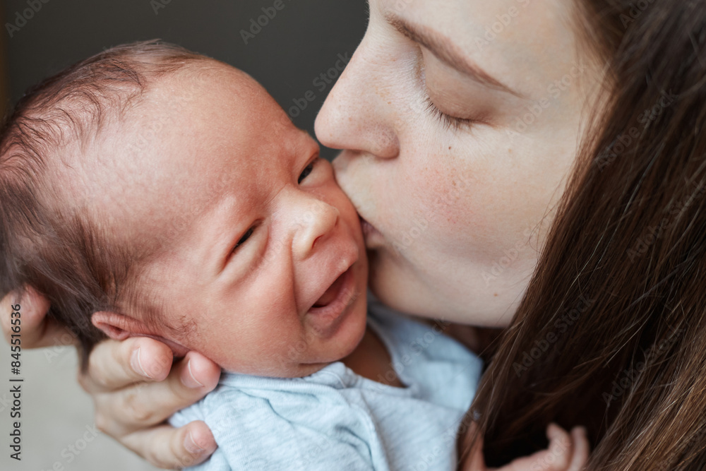 Gentle Caucasian brown haired young mom is nursing her healthy newborn woman kissing her crying tiny kid with love baby resting peacefully in his mother's arms Gentle Caucasian brown haired young mom is nursing her healthy newborn woman kissing her crying tiny kid with love baby resting peacefully in his mother's arms