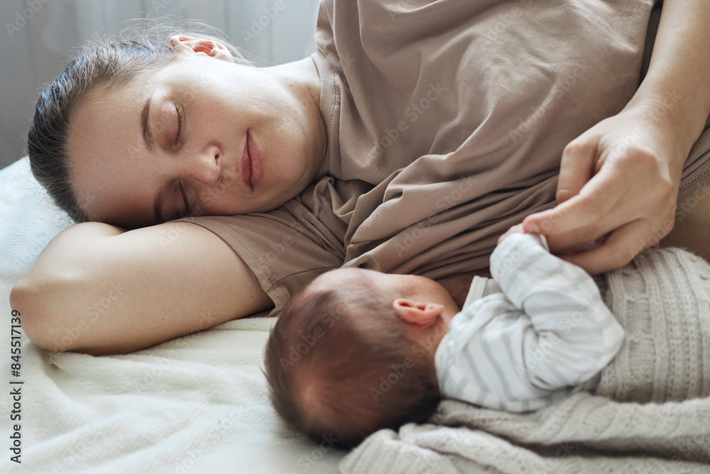 Breastfeeding at home. At-home lactation. Sleepy tired mother breastfeeding her baby while lying on bed with closed eyes resting relaxing Breastfeeding at home. At-home lactation. Sleepy tired mother breastfeeding her baby while lying on bed with closed eyes resting relaxing