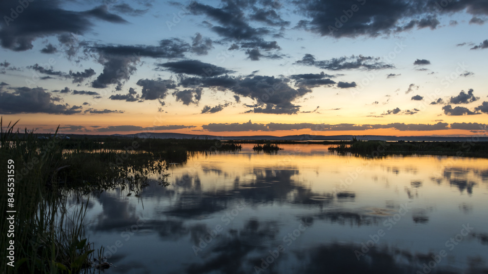 Fototapeta premium The banner is a beautiful sunset on the background of a pond with vegetation in the rays of the setting sun.
