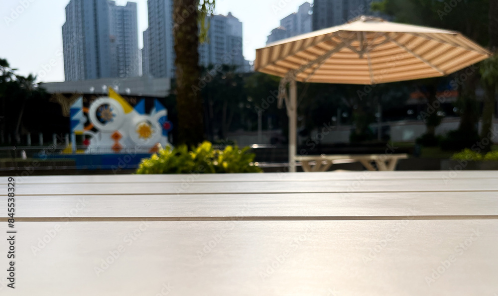 Fototapeta premium Close up selective focus on outdoor wooden table surface isolated on urban city buildings, trees, and umbrella on horizontal ratio background photography.