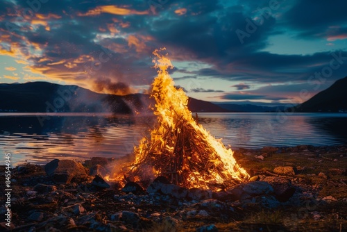 Experience the vibrant energy of the Midnight Sun Party in Norway as the dancing flames of a bonfire illuminate the night sky against the mesmerizing backdrop of the midnight sun.