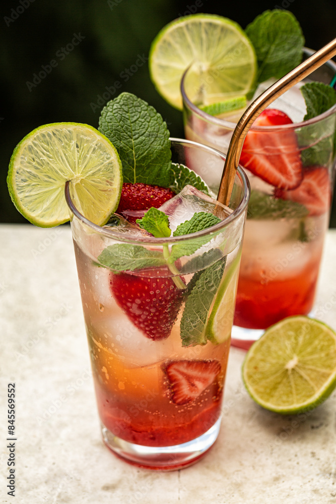 Strawberry mojito. Cold fresh drink in a glass, green outdoor on background. Refreshing summer cocktail with strawberries, lime, mint leaves, ice cubes. Vertical image. Strawberry mojito. Cold fresh drink in a glass, green outdoor on background. Refreshing summer cocktail with strawberries, lime, mint leaves, ice cubes. Vertical image.