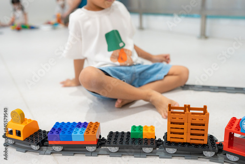 Happy kindergarten asian boy enjoying play colorful toy train block on white lession room photo