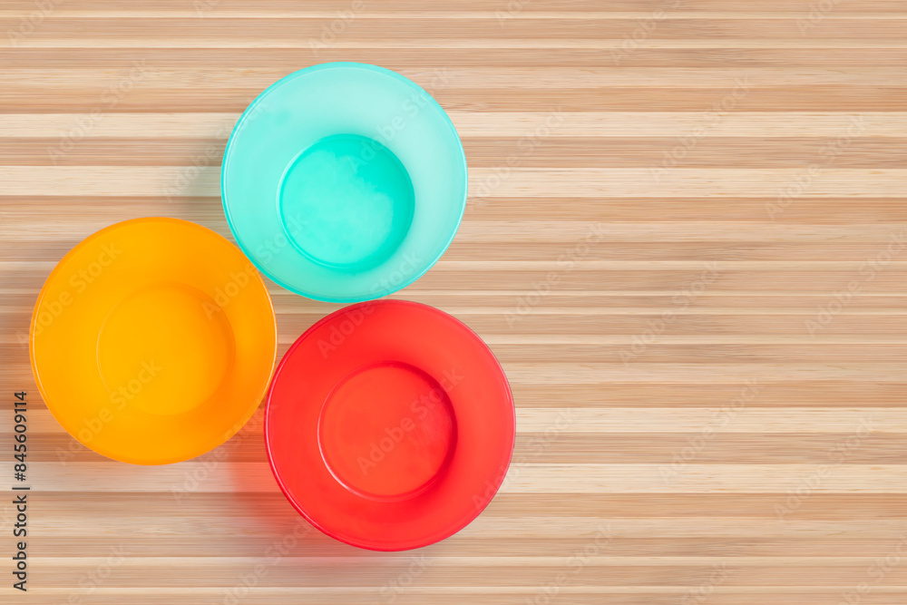 Three different colored plastic empty bowl on wooden table. Three different colored plastic empty bowl on wooden table.