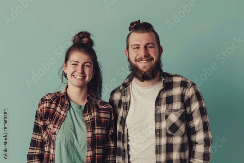 Portrait of a jovial couple in their 30s dressed in a relaxed flannel shirt in front of soft teal background
