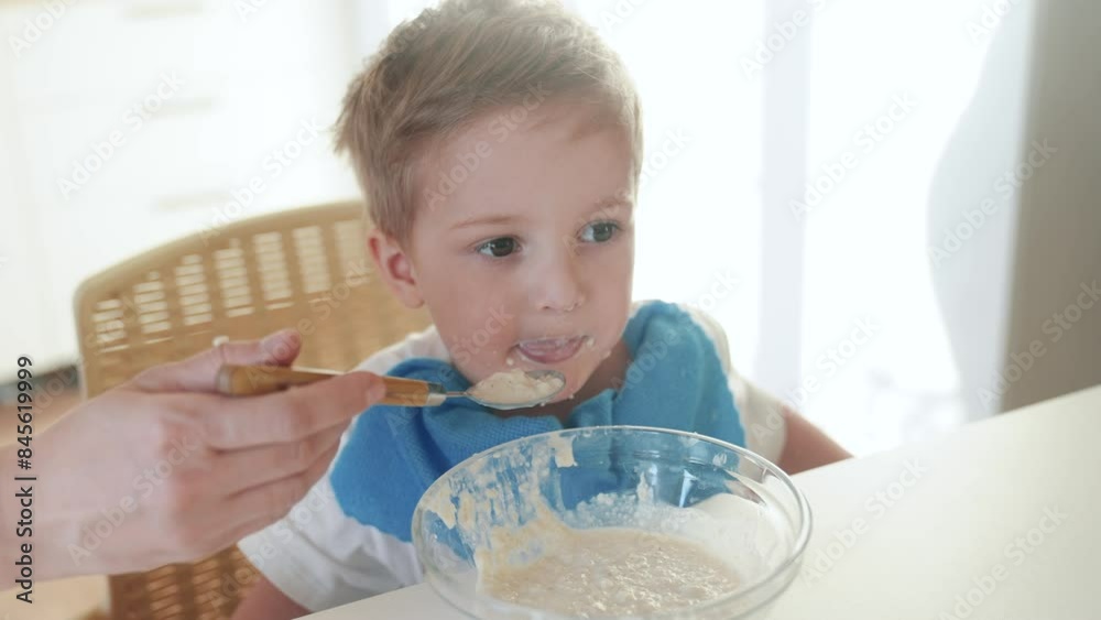 mother feeds porridge to her son. happy family healthy food concept. the boy little son eats porridge with a spoon soiled in his face. child dirty dirty funny lifestyle eating porridge himself video mother feeds porridge to her son. happy family healthy food concept. the boy little son eats porridge with a spoon soiled in his face. child dirty dirty funny lifestyle eating porridge himself video