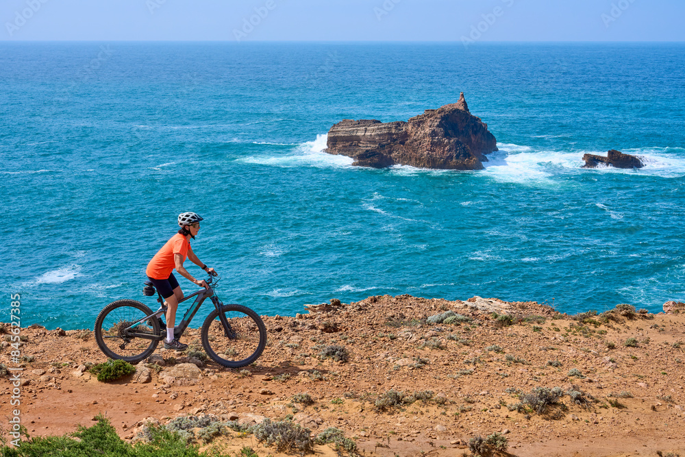 Fototapeta premium happy active senior woman cycling on the the rocky cliffs of the Vicentina coast of Algarve, Portugal near Sagres and Vila do Bispo