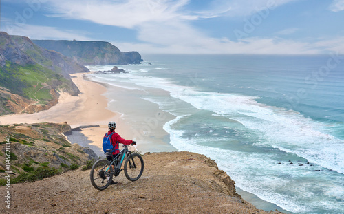 happy active senior woman cycling on the the rocky cliffs of the Vicentina coast of  Algarve, Portugal near Sagres and Vila do Bispo 