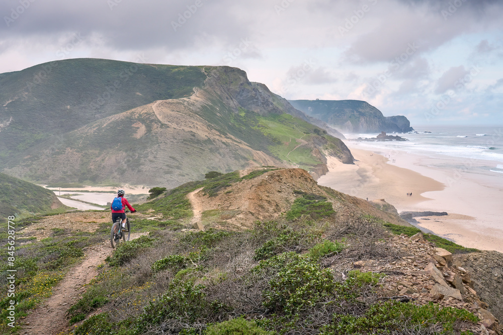 Obraz premium happy active senior woman cycling on the the rocky cliffs of the Vicentina coast of Algarve, Portugal near Sagres and Vila do Bispo 