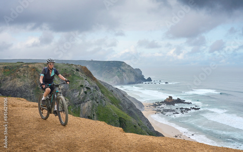happy active senior woman cycling on the the rocky cliffs of the Vicentina coast of  Algarve, Portugal near Sagres and Vila do Bispo 