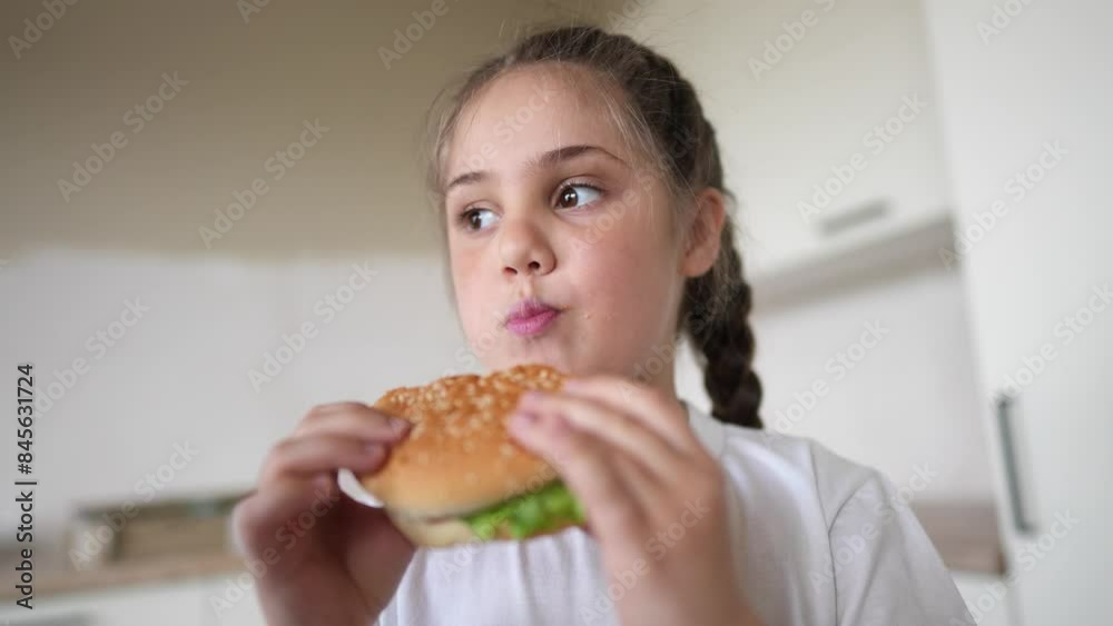 little kid girl eating a hamburger. unhealthy fast food meal proper nutrition concept. child greedily with pleasure bites a big burger in the kitchen at home. kid lifestyle eats fast food close-up little kid girl eating a hamburger. unhealthy fast food meal proper nutrition concept. child greedily with pleasure bites a big burger in the kitchen at home. kid lifestyle eats fast food close-up