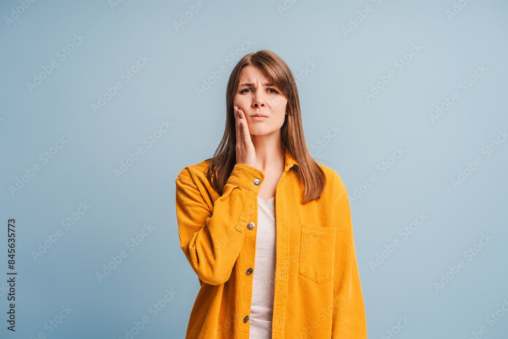 Sad upset middle aged woman touching cheek, having toothache isolated on blue background Sad upset middle aged woman touching cheek, having toothache isolated on blue background