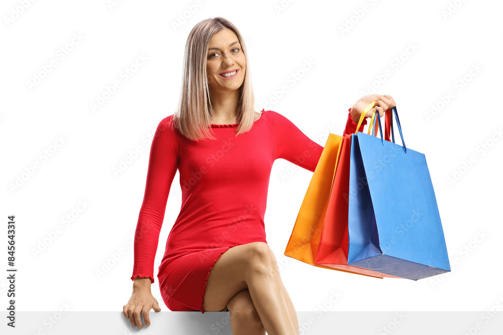 Blond attractive woman in a red dress sitting on a panel with shopping bags Blond attractive woman in a red dress sitting on a panel with shopping bags