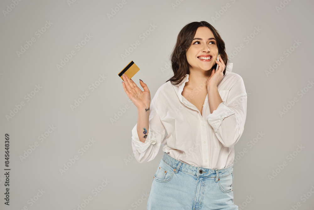 A stylish plus size woman multitasking, holding a credit card and talking on a cell phone against a gray backdrop. A stylish plus size woman multitasking, holding a credit card and talking on a cell phone against a gray backdrop.