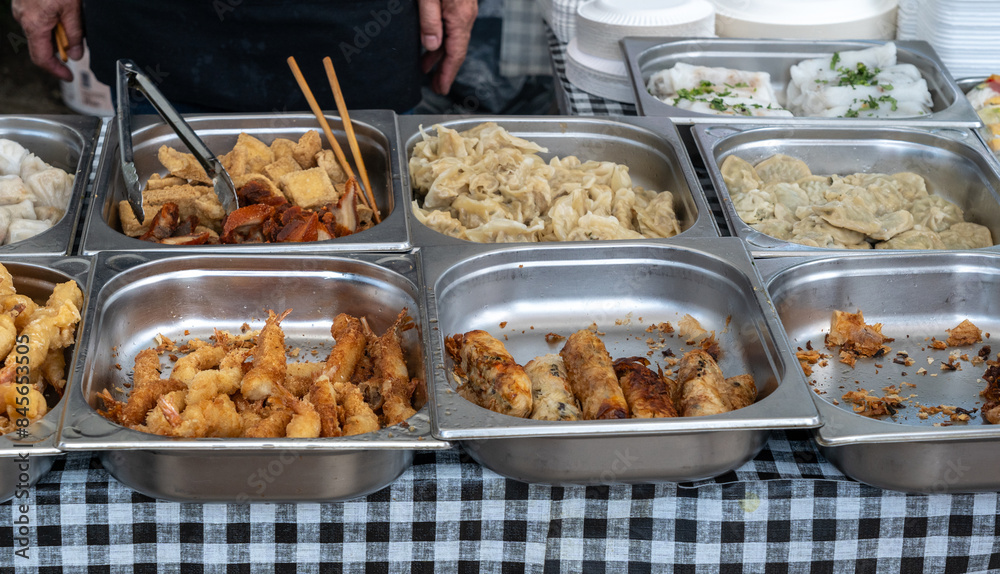 Assorted Asian street food in stainless steel trays, fried squid, various dumplings, spring rolls at food market Assorted Asian street food in stainless steel trays, fried squid, various dumplings, spring rolls at food market