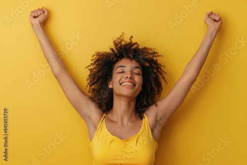 Woman With Curly Hair Smiles With Arms Raised In Front Of Yellow Background