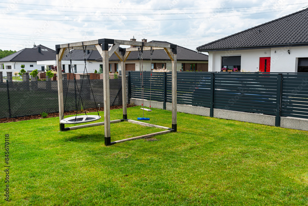 A modern, square-shaped wooden playground, made of metal corners, standing on the lawn in the yard. A modern, square-shaped wooden playground, made of metal corners, standing on the lawn in the yard.
