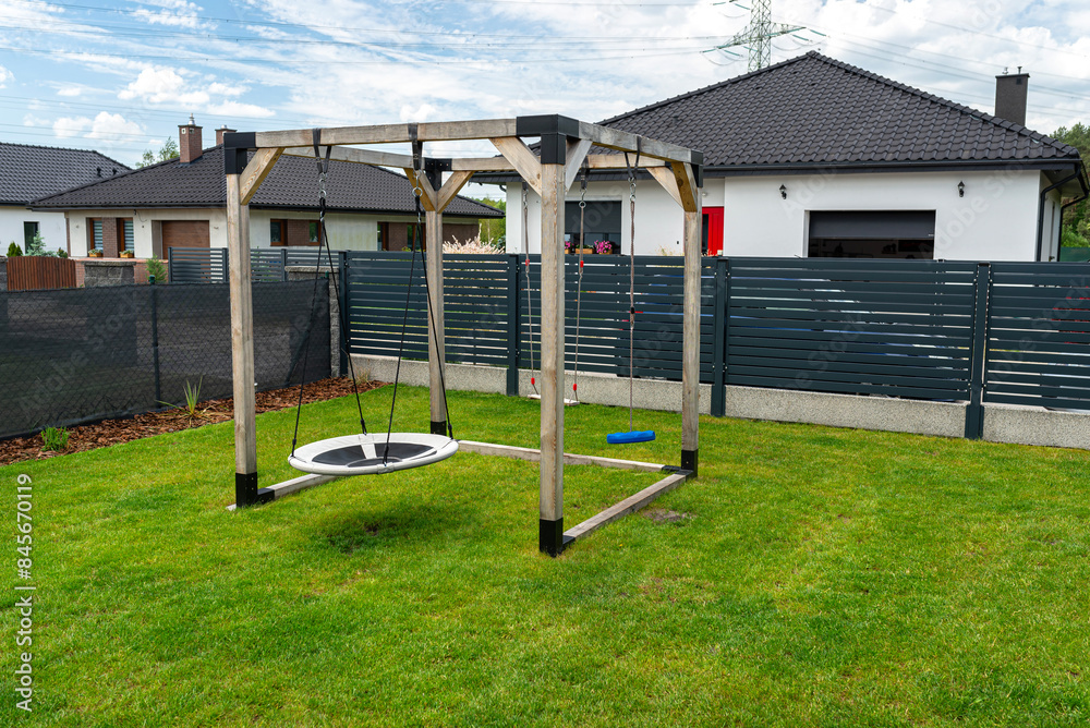 A modern, square-shaped wooden playground, made of metal corners, standing on the lawn in the yard. A modern, square-shaped wooden playground, made of metal corners, standing on the lawn in the yard.