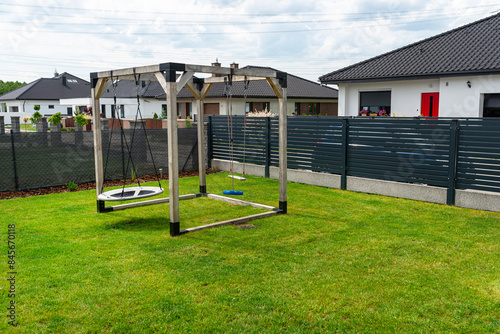 A modern, square-shaped wooden playground, made of metal corners, standing on the lawn in the yard.