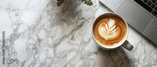 Top View of a Coffee Cup With Latte Art, Laptop, and Greenery on a White Table