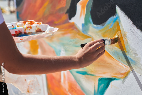 Fototapeta Naklejka Na Ścianę i Meble -  Female painter hand passionately paints picture with paintbrush for outdoor street exhibition using vibrant colors, close up view