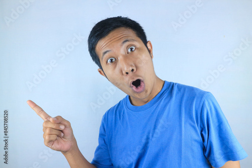 funny facial expression of shocked young asian man pointing side direction, promoting product photo