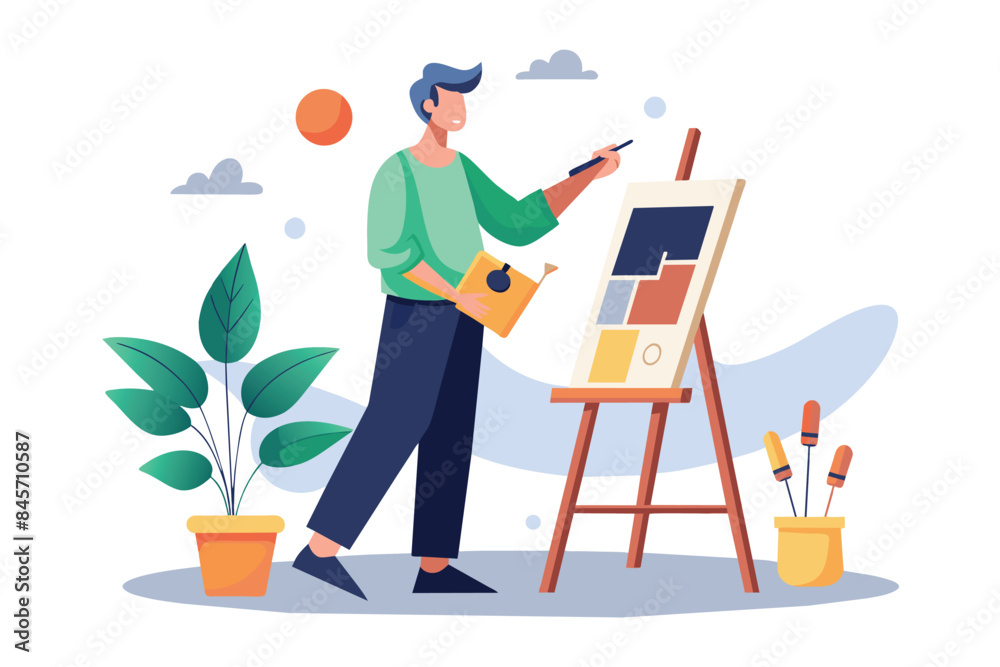 Fototapeta premium A man in green shirt and black pants paints a colorful design on a canvas using a paintbrush. He holds a yellow book in his left hand.