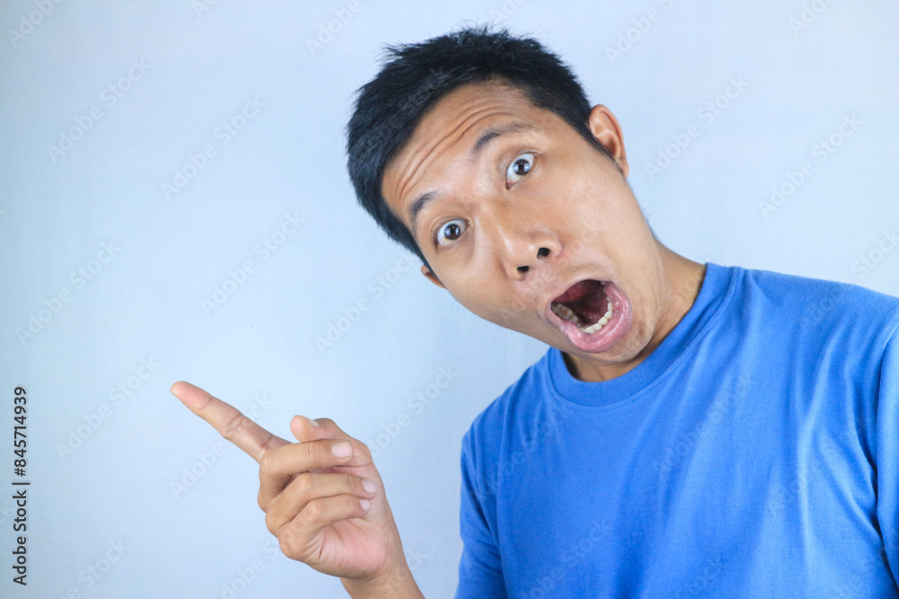 funny facial expression of shocked young asian man pointing side direction, promoting product funny facial expression of shocked young asian man pointing side direction, promoting product