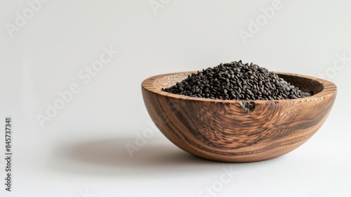 Wooden bowl containing black sesame seeds against a white backdrop