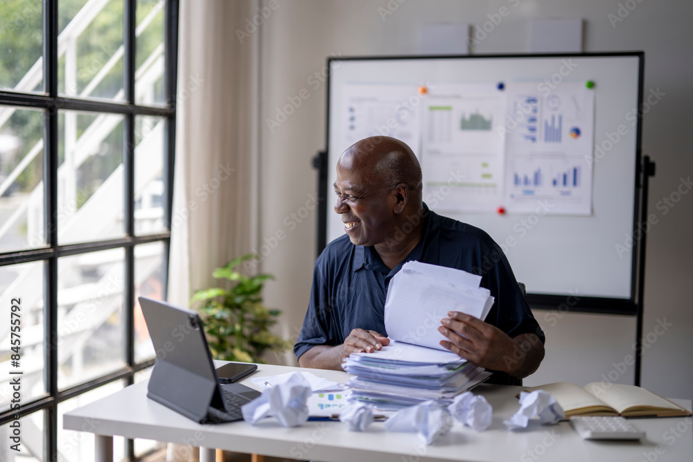 A man is sitting at a desk with a laptop and a stack of papers A man is sitting at a desk with a laptop and a stack of papers