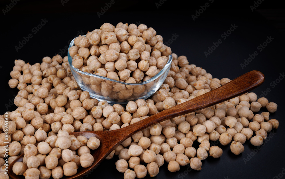 Glass cup with chickpeas. Wooden spoon with chickpeas and chickpeas scattered around. Glass cup with chickpeas. Wooden spoon with chickpeas and chickpeas scattered around.