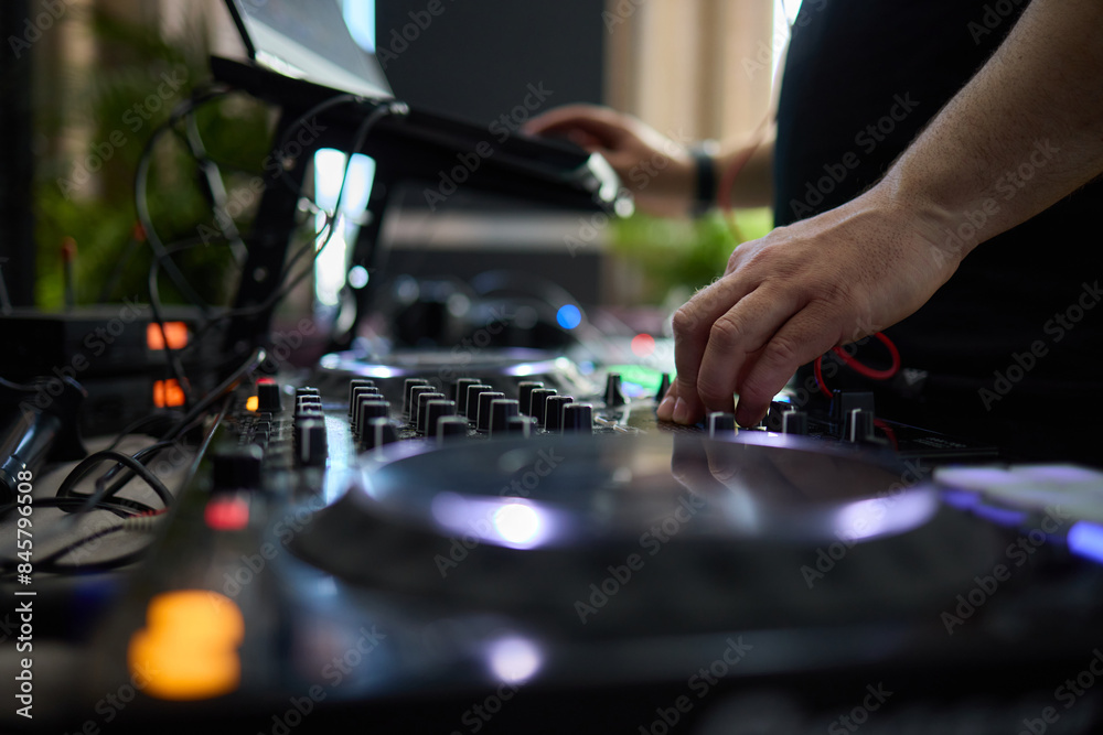 control DJ for mixing music with blurred people dancing at party in nightclub.
