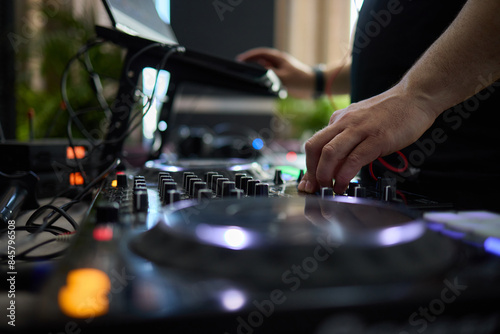 control DJ for mixing music with blurred people dancing at party in nightclub.