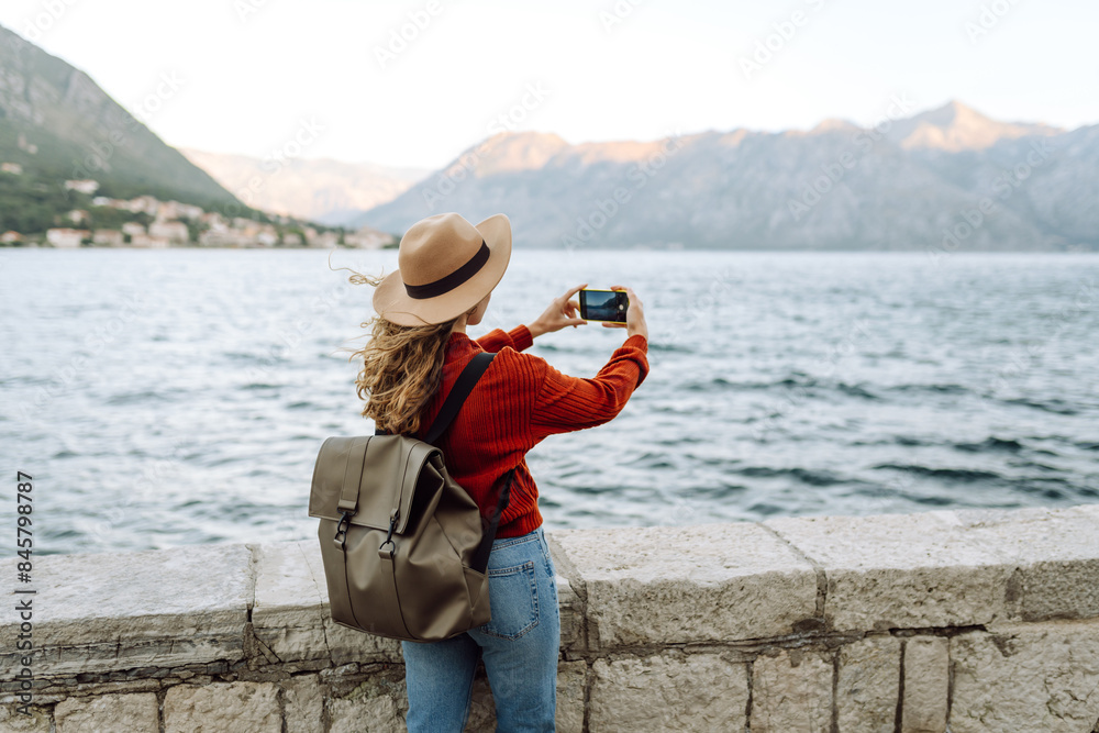 Obraz premium Travel blogger takes photos on the camera of smartphone amazing landscape with mountains, ocean and sunset sky on smartphone during vacation. Tourist during holidays