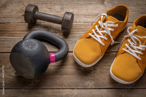 small iron kettlebell and dumbbell with barefoot sneakers on a rustic wooden deck, fitness concept photo