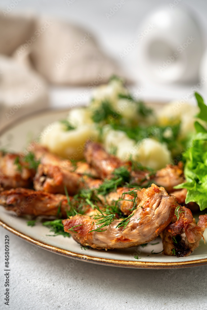 Baked or fried chicken necks in barbecue sauce, cauliflower and lettuce leaves on a plate on the table. A healthy dinner on a light gray background in closeup. Proper nutrition Baked or fried chicken necks in barbecue sauce, cauliflower and lettuce leaves on a plate on the table. A healthy dinner on a light gray background in closeup. Proper nutrition