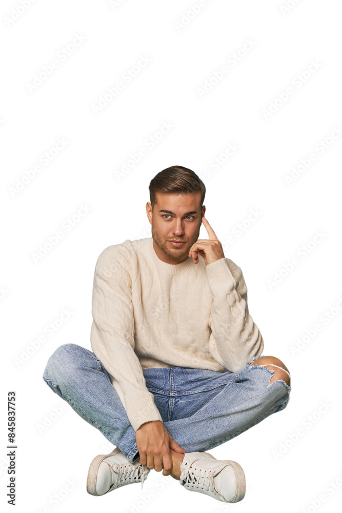 Young Caucasian man sitting on the floor in a studio setting Young Caucasian man sitting on the floor in a studio setting