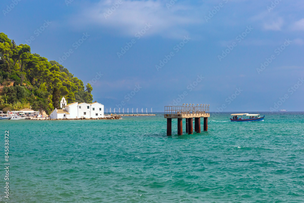 Fototapeta premium Vlacherna Monastery on the coast of Corfu, Greece, with boat passing by and clear blue waters