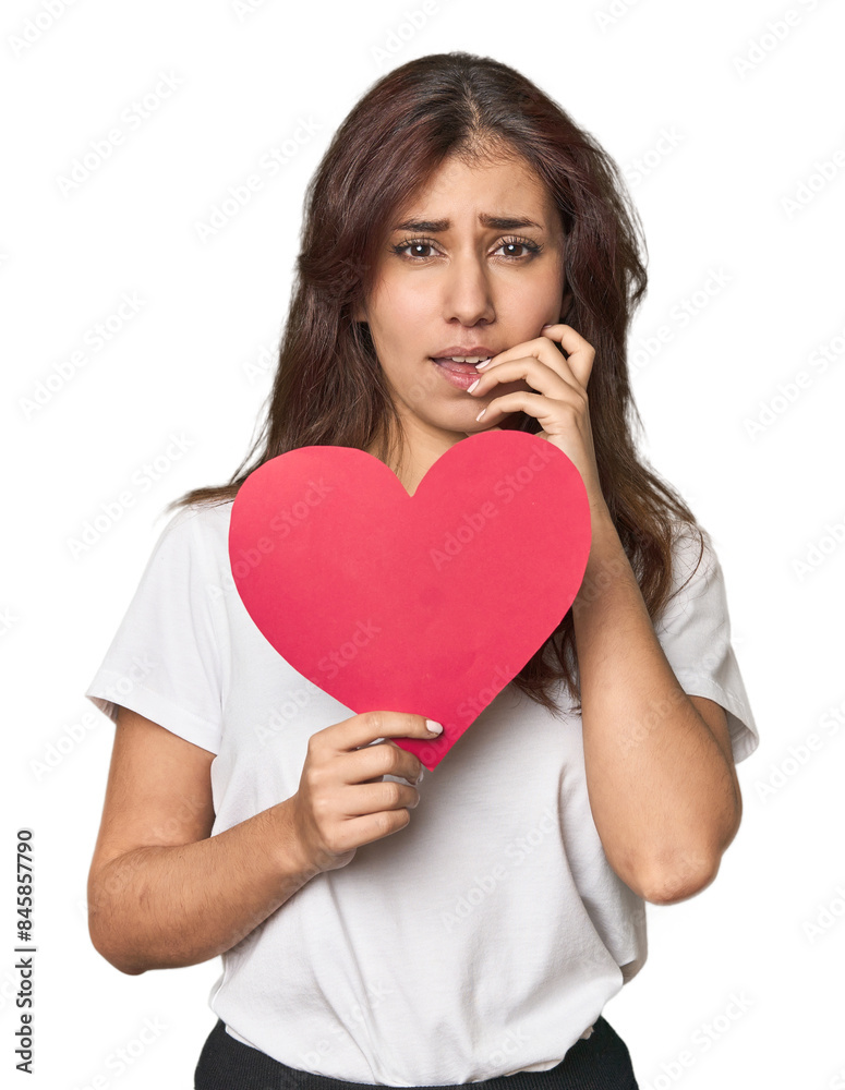 Middle Eastern woman holding paper heart biting fingernails, nervous and very anxious. Middle Eastern woman holding paper heart biting fingernails, nervous and very anxious.
